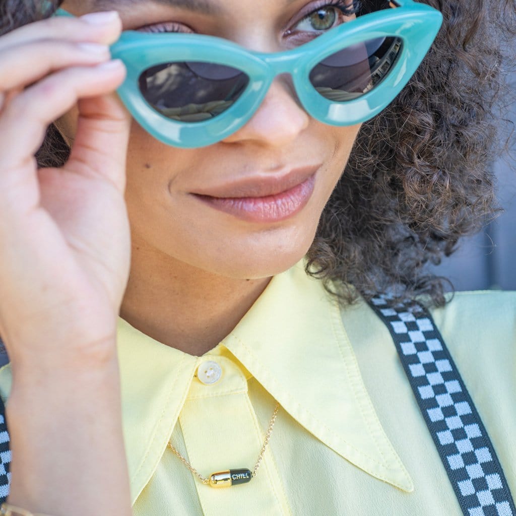 Woman with curly hair in turquoise cat-eye sunglasses and a yellow shirt wearing the Big Chill Pill Chain Necklace