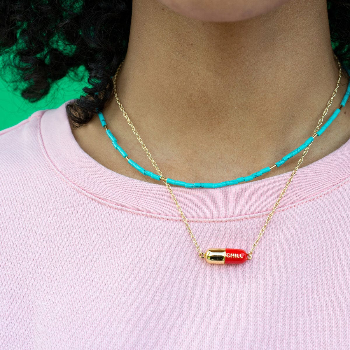 Woman in a pink top wearing the red Big Chill Pill Chain Necklace layered with a turquoise beaded necklace