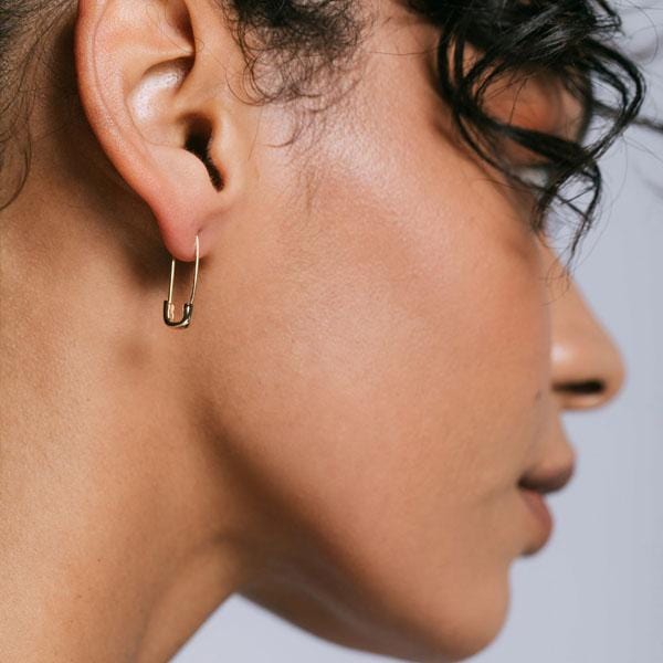 Woman with curly dark hair wearing a gold Classic Safety Pin Hoop