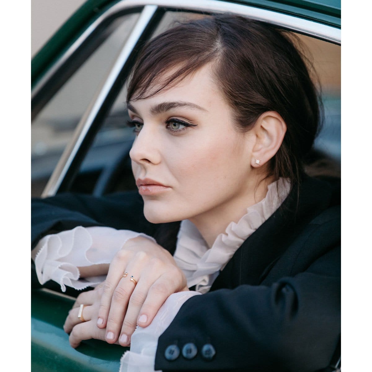 Woman with dark hair leaning on a car window, wearing gold Starburst Crystal Studs
