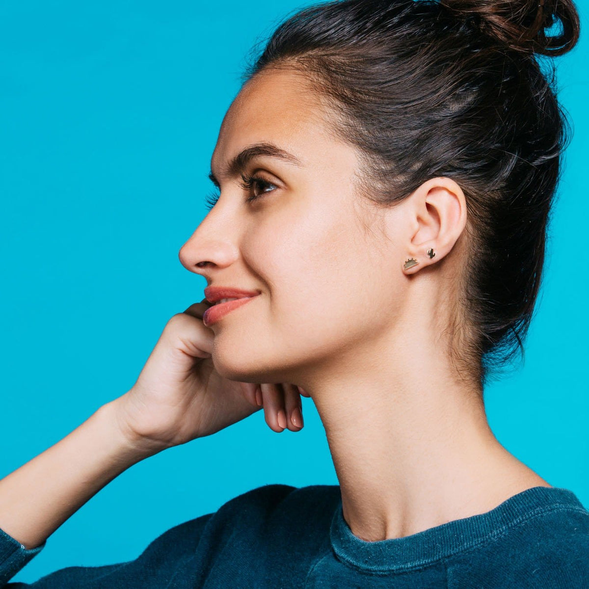 Woman with dark hair in a bun, hand at her chin, wearing a gold Cactus Stud