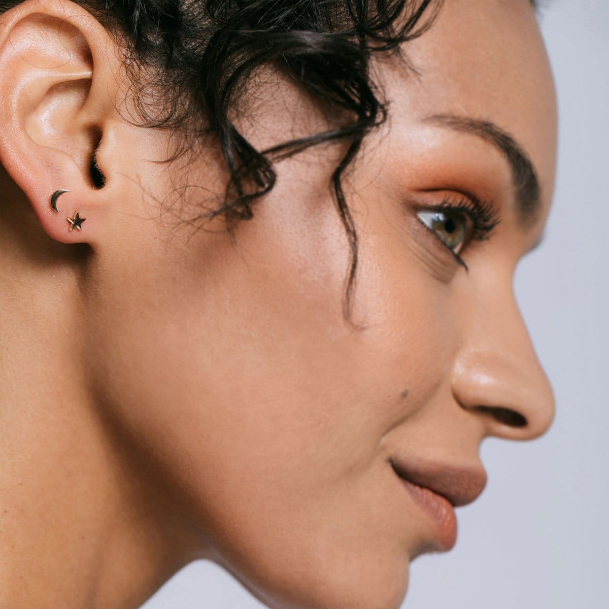 Profile of a woman with curly dark hair wearing gold Star and Moon Studs