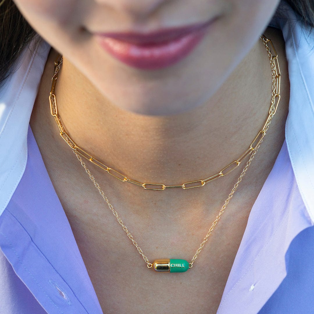 Smiling woman wearing the emerald Big Chill Pill Chain Necklace layered with a gold chain